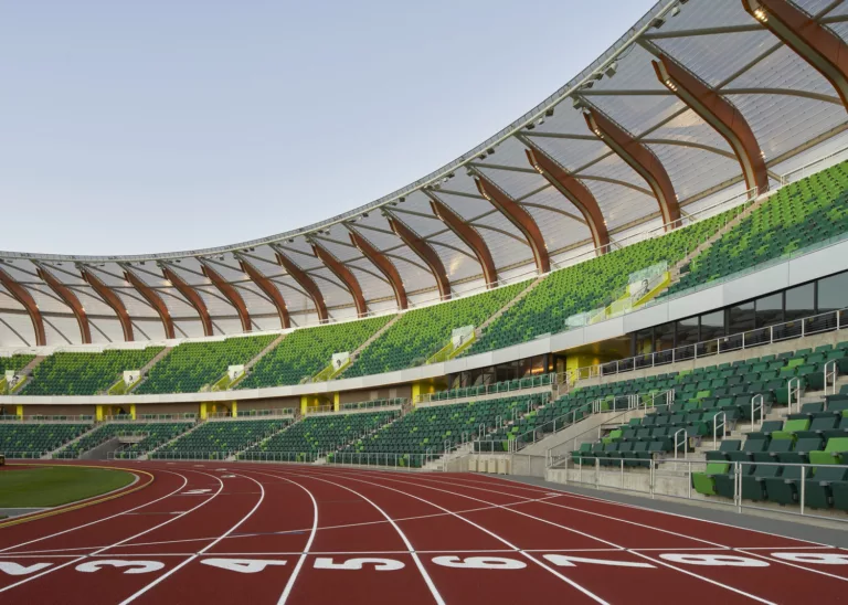 Daylight view of the University of Oregon’s Hayward Stadium looking up from the track-and-field lanes toward the green bleacher seating and unique glulam-and-steel composite canopy roof structure