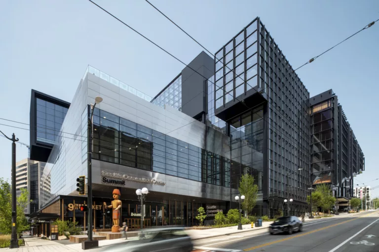 Exterior daylight view of the Seattle Convention Center Addition's southwest corner with interlocking steel-and-glass "boxes" comprising the structure and a 20-foot-tall Coast Salish welcome figure made of Western red cedar