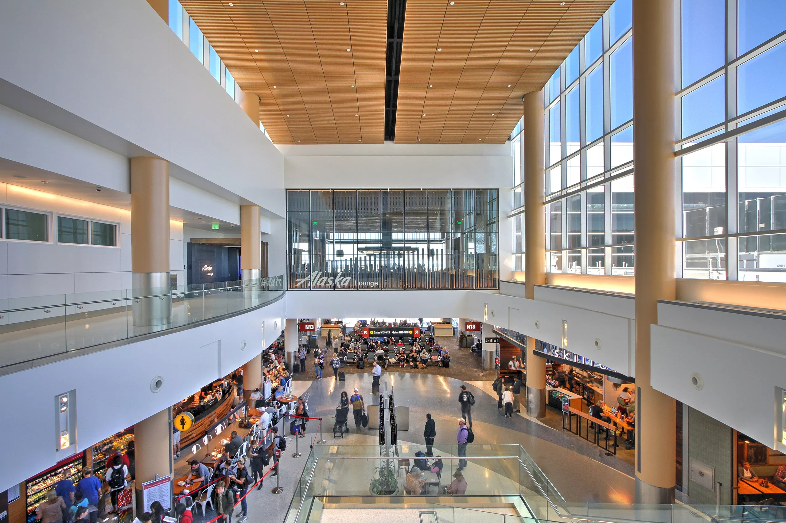 Interior view of the Sea-Tac International Airport North Satellite Modernization Project with the glass-enclosed Alaska Lounge above a concourse filled with travelers and shops