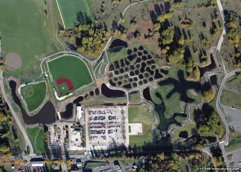 Overhead daylight view of the Magnuson Park wetlands, parking lot, pedestrian trails, and surrounding athletic fields for baseball, softball, and soccer