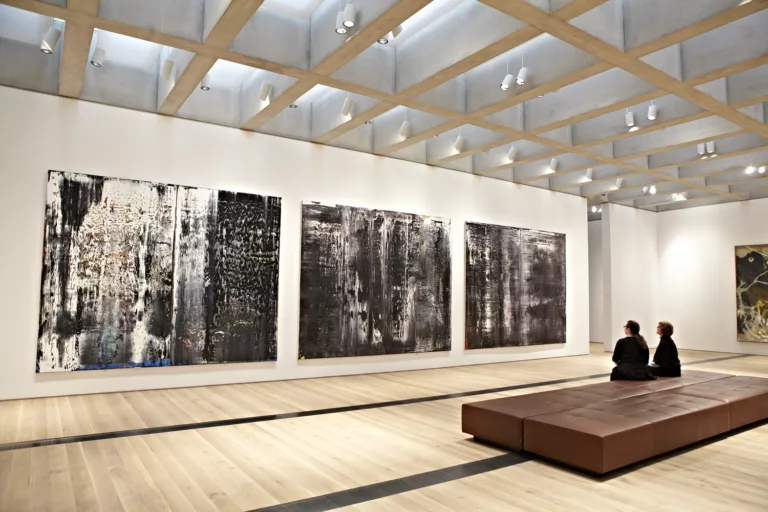 Interior view of a new gallery inside the renovated and expanded St. Louis Art Museum with two visitors seated and viewing wall-hung paintings