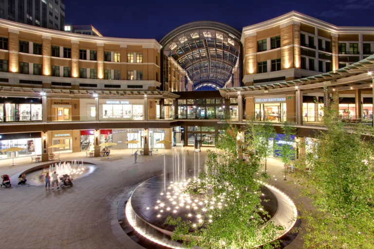 Exterior twilight view of City Creek Center’s illuminated Richards Court Fountain and Galleria with two levels of retail shops, two levels of office space, and an arched glass roof