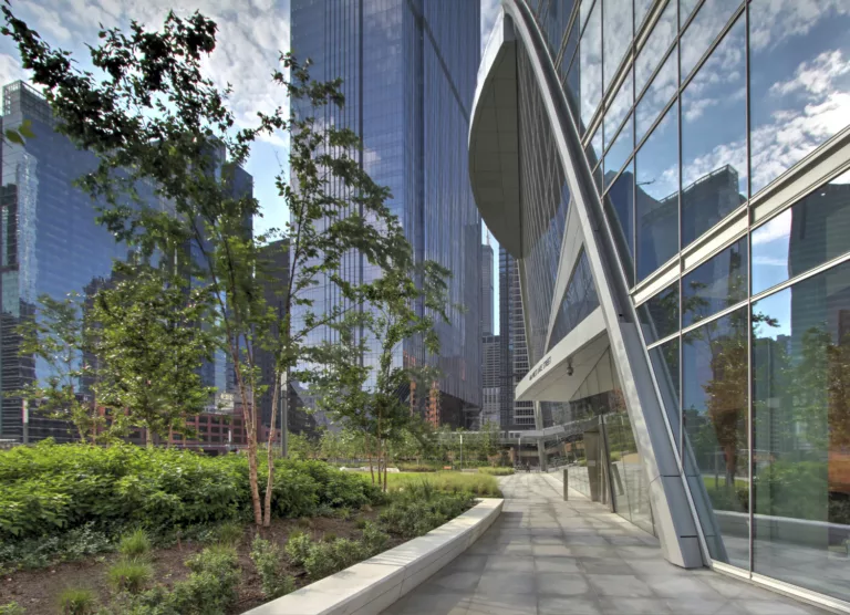 Exterior daylight view of River Point Tower's landscaped plaza featuring the sloping, glass-and-steel entrance