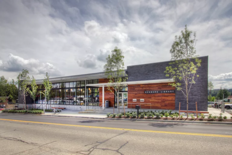 Exterior daylight view of Kenmore Library's north entrance with sidewalk landscaping, trees, steps, and bike racks