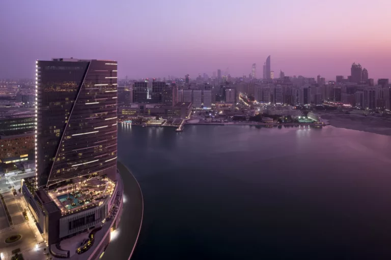 Aerial nighttime view of the illuminated Rosewood Hotel & Residences tower rising 38 stories above the waterfront with distant views of Abu Dhabi's skyline