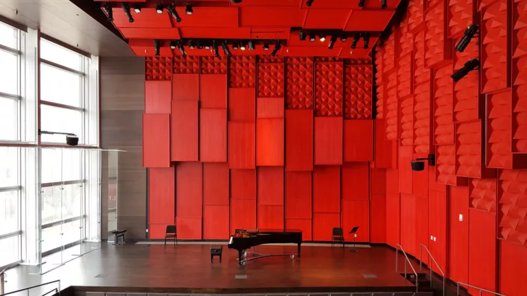 Interior view of the University of Iowa Voxman School of Music's small recital hall with a piano center stage surrounded by bright red acoustic walls