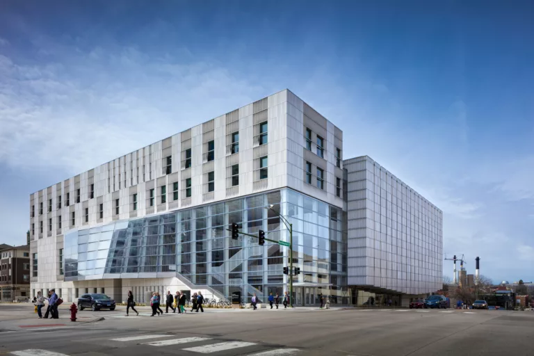 Exterior daylight view of the University of Iowa Voxman School of Music and its glass-enclosed lobby with pedestrians crossing the street