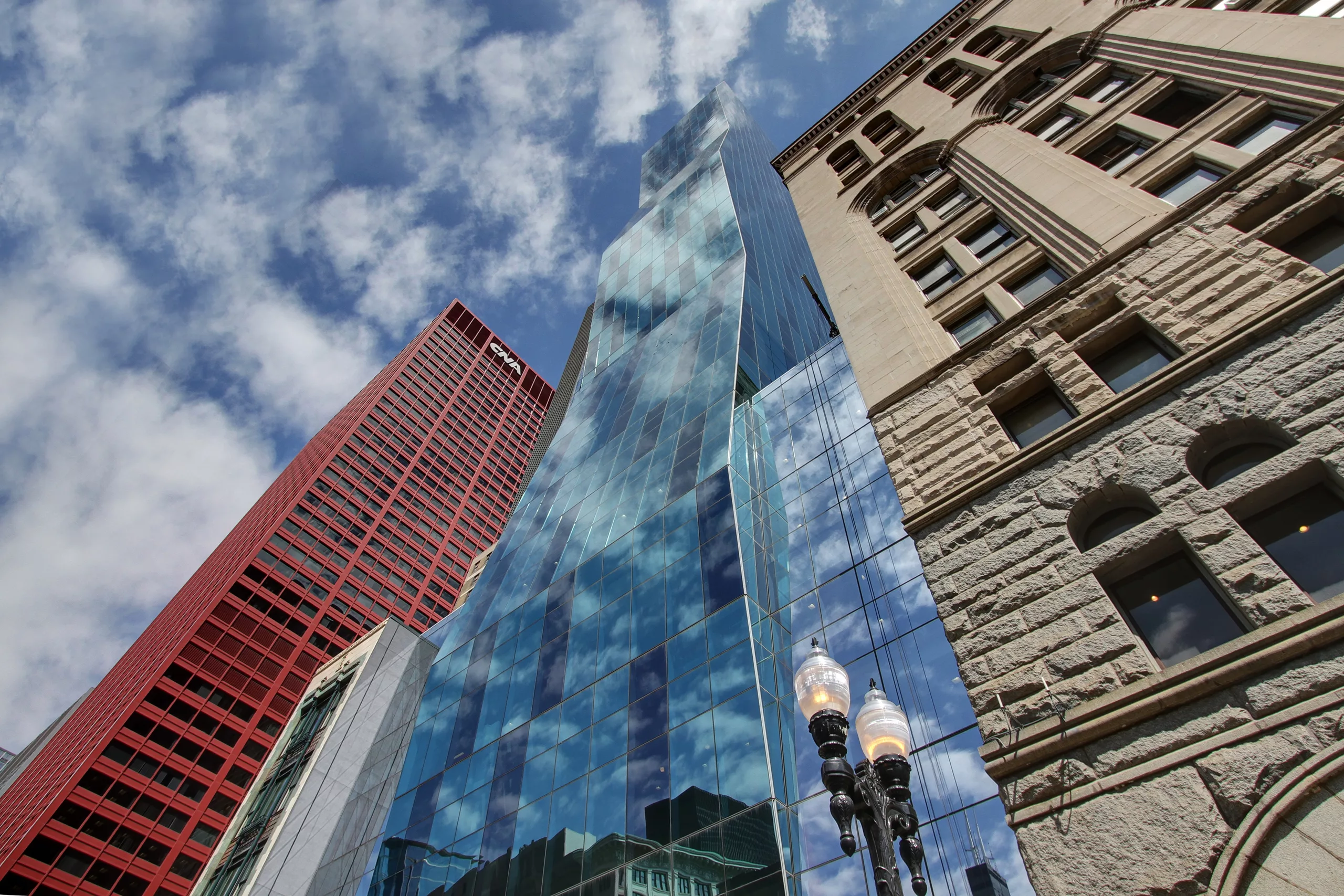 Exterior daylight view looking up at the angular facade of the Roosevelt University Wabash Building wedged between a historical building to the right, a modern skyscraper to the left, and an ornate streetlamp below