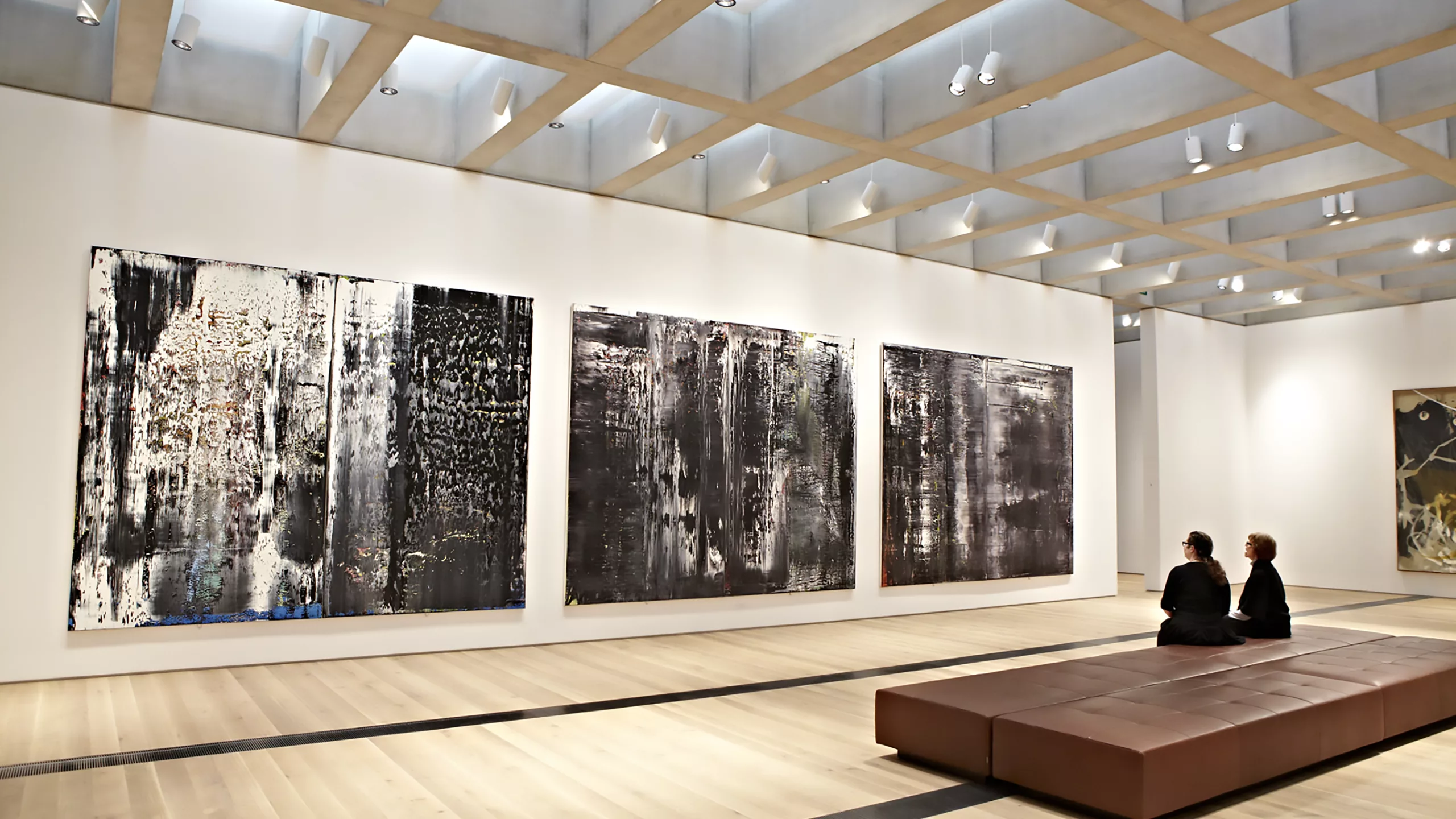 Interior view of a new gallery inside the renovated and expanded St. Louis Art Museum with two visitors seated and viewing wall-hung paintings