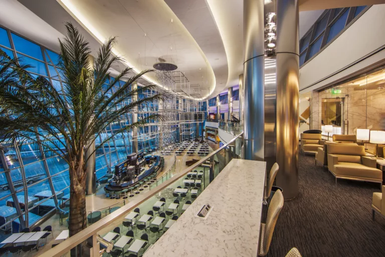 Interior evening image of the downstairs dining hall and an upstairs lounge  with an indoor palm tree and ceiling-mounted, cube-shaped public art at San Diego International Airport Terminal 2 West