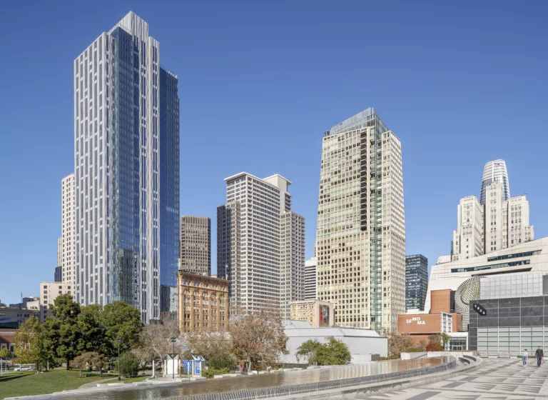 Exterior daylight view of the 40-story glass-and-steel 706 Mission Building and the adjacent 10-story heritage Aronson Building with a park, water feature, and pedestrian plaza in the foreground and surrounding high-rise buildings downtown