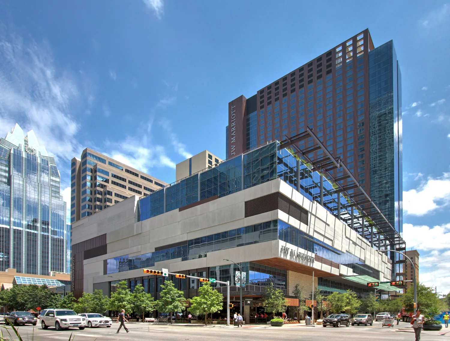 Daylight view looking across the street at the 35-story JW Marriott Austin rising from a six-story podium surrounded by roadway traffic and nearby high-rise buildings