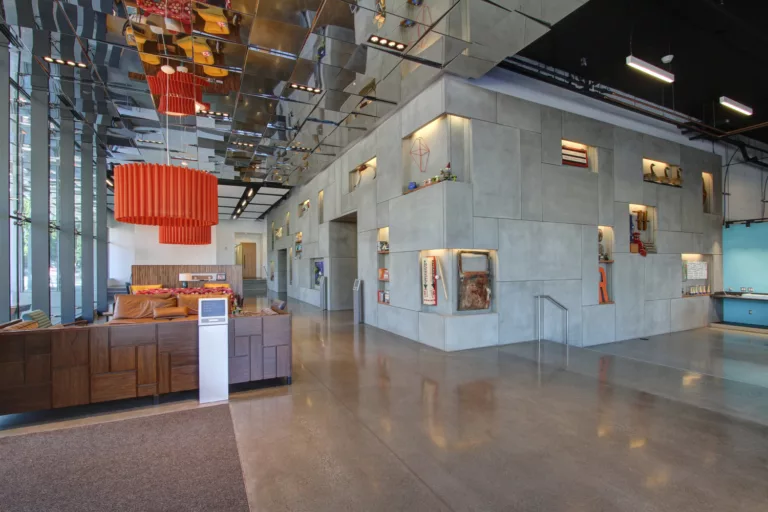 Interior daylight view of the Hill7 hotel lobby with couch seating, hanging decorative lights, a shallow staircase, and public art on the walls