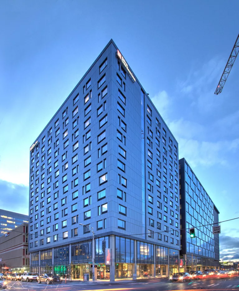 Exterior twilight view of the 14-story hotel and 12-story office tower comprising Hill7 with headlights of surrounding roadway vehicle traffic