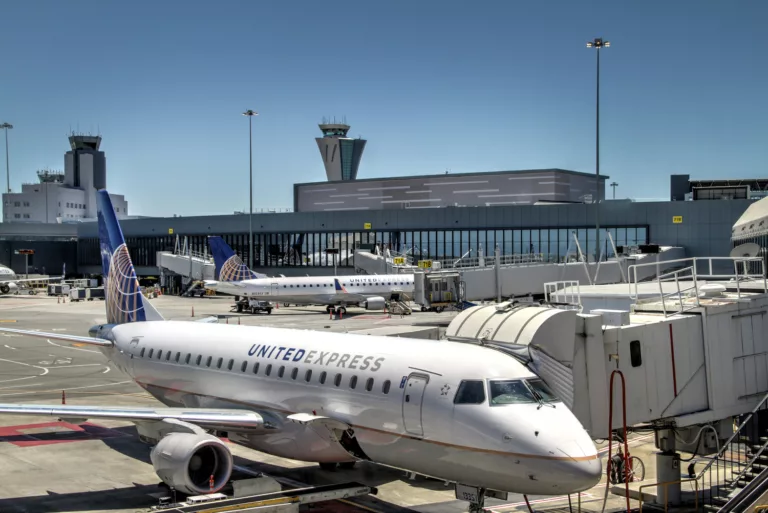 Exterior daylight view of San Francisco International Airport's Terminal 3 East Retrofit and Expansion with two airplanes parked at gates and distant air traffic control towers