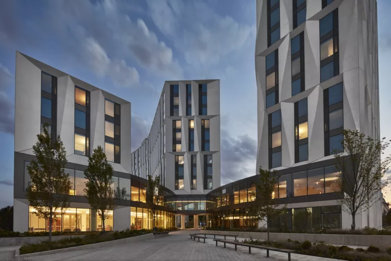 Exterior twilight view of the University of Chicago's North Residence Hall with three mid-rise buildings illuminated within and an outdoor plaza containing benches and minimal landscaping with trees
