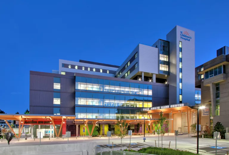 Exterior twilight view of the eight-story BC Children’s Hospital TECK Acute Care Centre with parking spaces and central lobby entrance