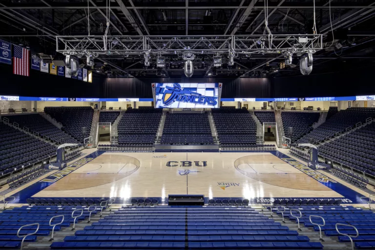 Interior view of the California Baptist University Arena's basketball court   featuring overhead rigging, a video board, and bleacher seating