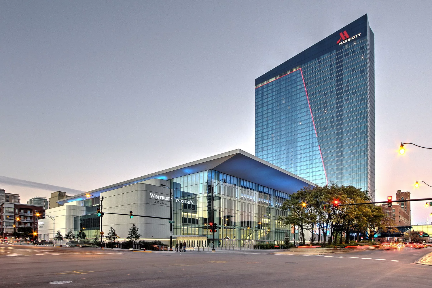 An exterior daylight view looking across the street at the Marriott Marquis at McCormick Place’s 40-story glass facade with prominent roofline signage and the six-story Wintrust Arena in the foreground