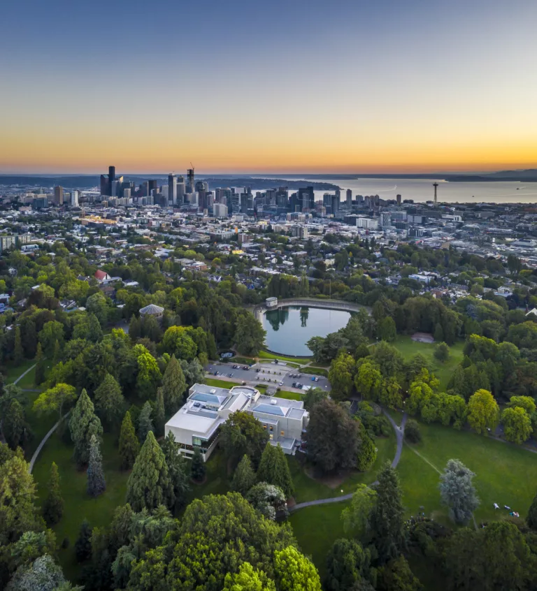Aerial view at sunset of the Seattle Asian Art Museum Expansion and surrounding Volunteer Park with the Space Needle, Elliott Bay, and the downtown skyline in the distance