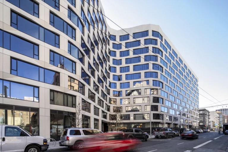 Exterior daylight view of the 12-story Serif Residences and The Line Hotel with street-level retail spaces and vehicles traveling along a four-lane road