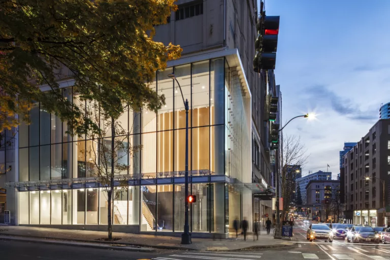 Exterior twilight view of the illuminated northeast entrance to Pacific Place featuring a four-story glass façade and vehicle traffic on adjacent Olive Way