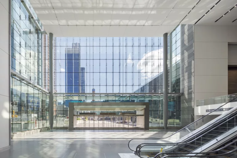 Interior daylight view of the Javits Convention Center Expansion's lobby with escalators and a wall of windows to reveal a high-rise building in the distance