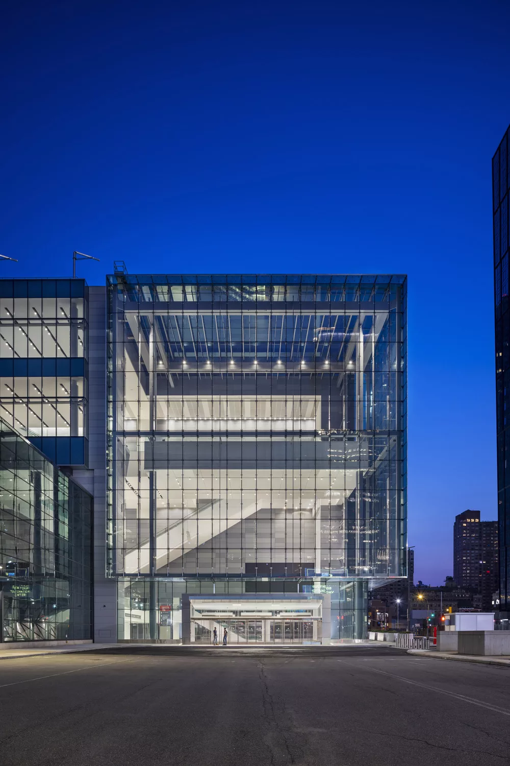 Exterior twilight view of the Javits Convention Center Expansion's soaring, glass-and-steel lobby illuminated within to reveal escalators and exhibit space