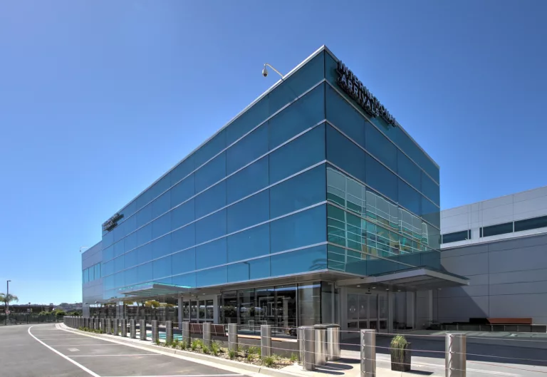 Exterior daylight view of San Diego International Airport's multi-story, glass-and-steel Federal Inspection Station fronted by steel safety bollards and minimal landscaping