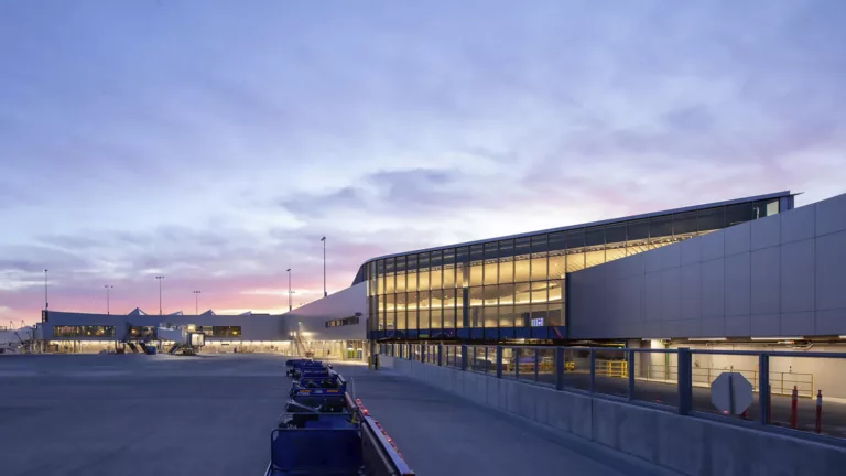 Exterior twilight view of Phoenix Sky Harbor International Airport's illuminated and glass-enclosed concourse expansion inside Terminal 4