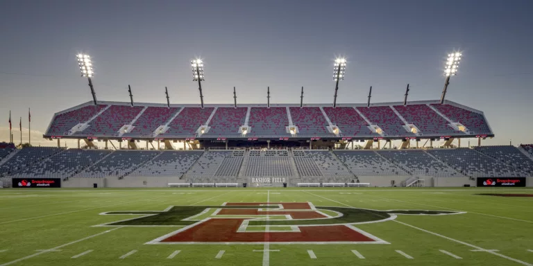 Field-level twilight view of the empty stands at San Diego State University’s Snapdragon Stadium featuring mounted field lighting and the team’s logo on the midfield turf