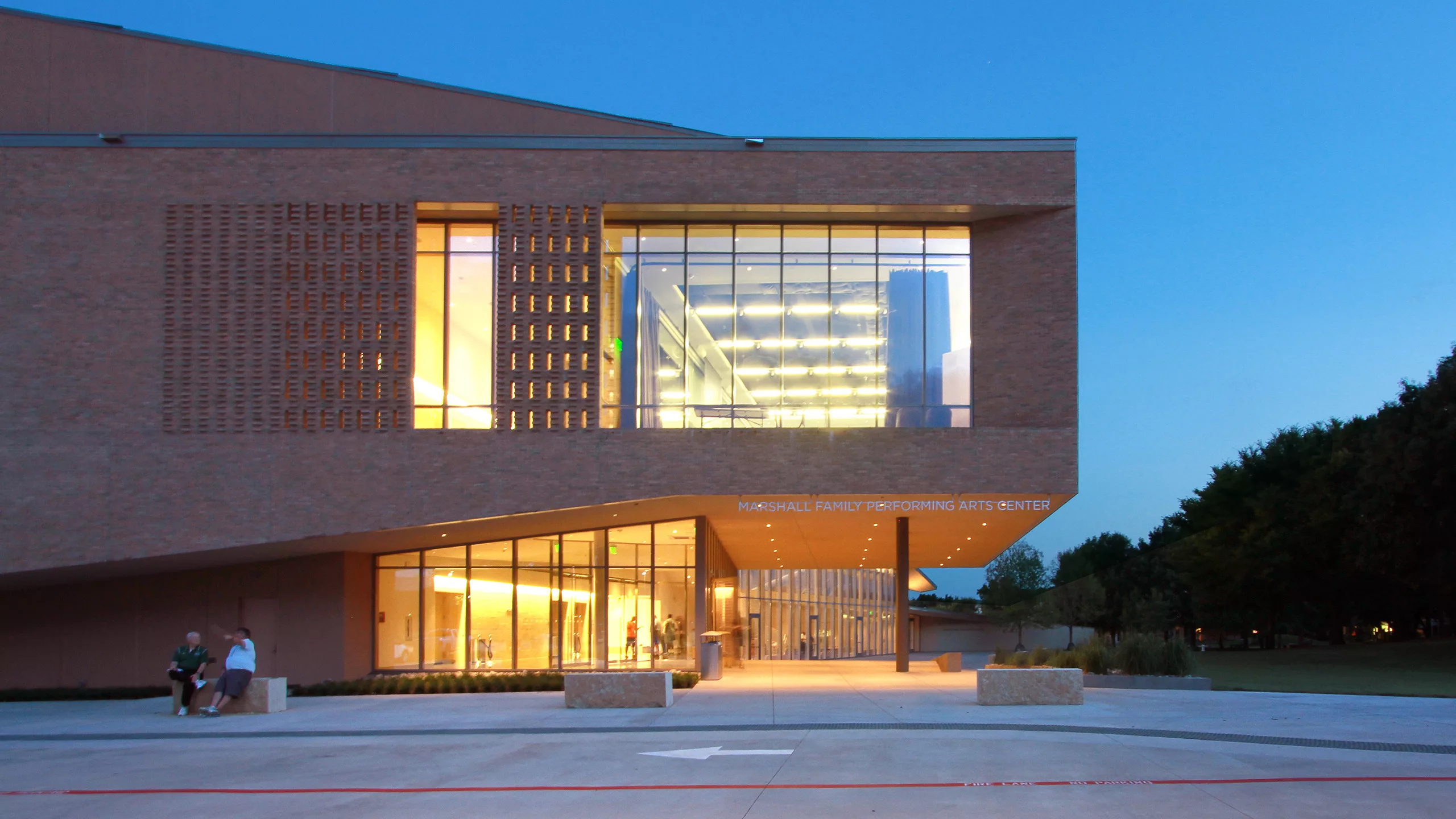 Exterior twilight view of the north side of Greenhill School Marshall Family Performing Arts Center's illuminated and glass-enclosed lobby