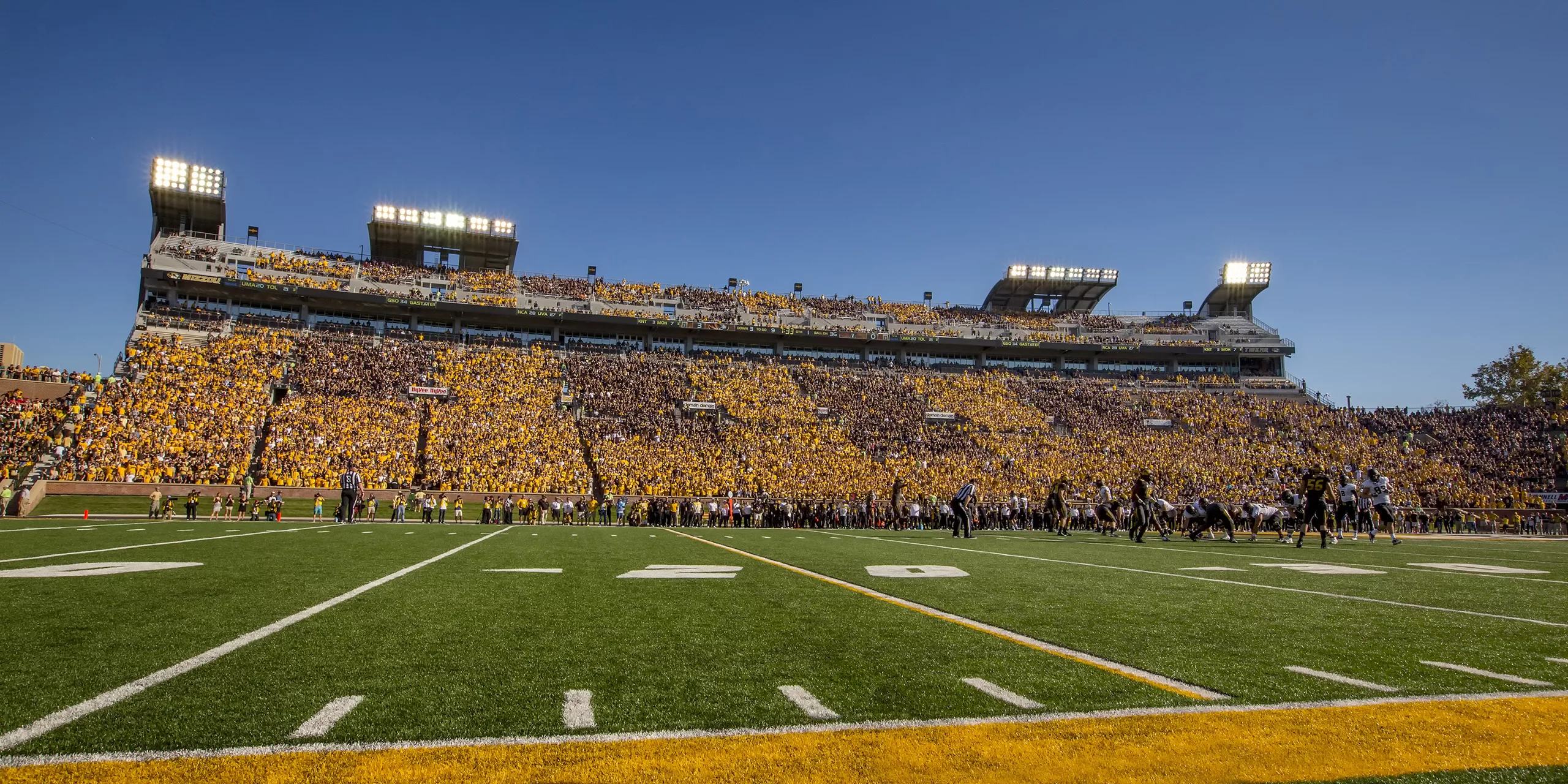 Exterior daylight view looking across the field during a football game at the University of Missouri's Memorial Stadium with a packed stadium in the distance and players on the field