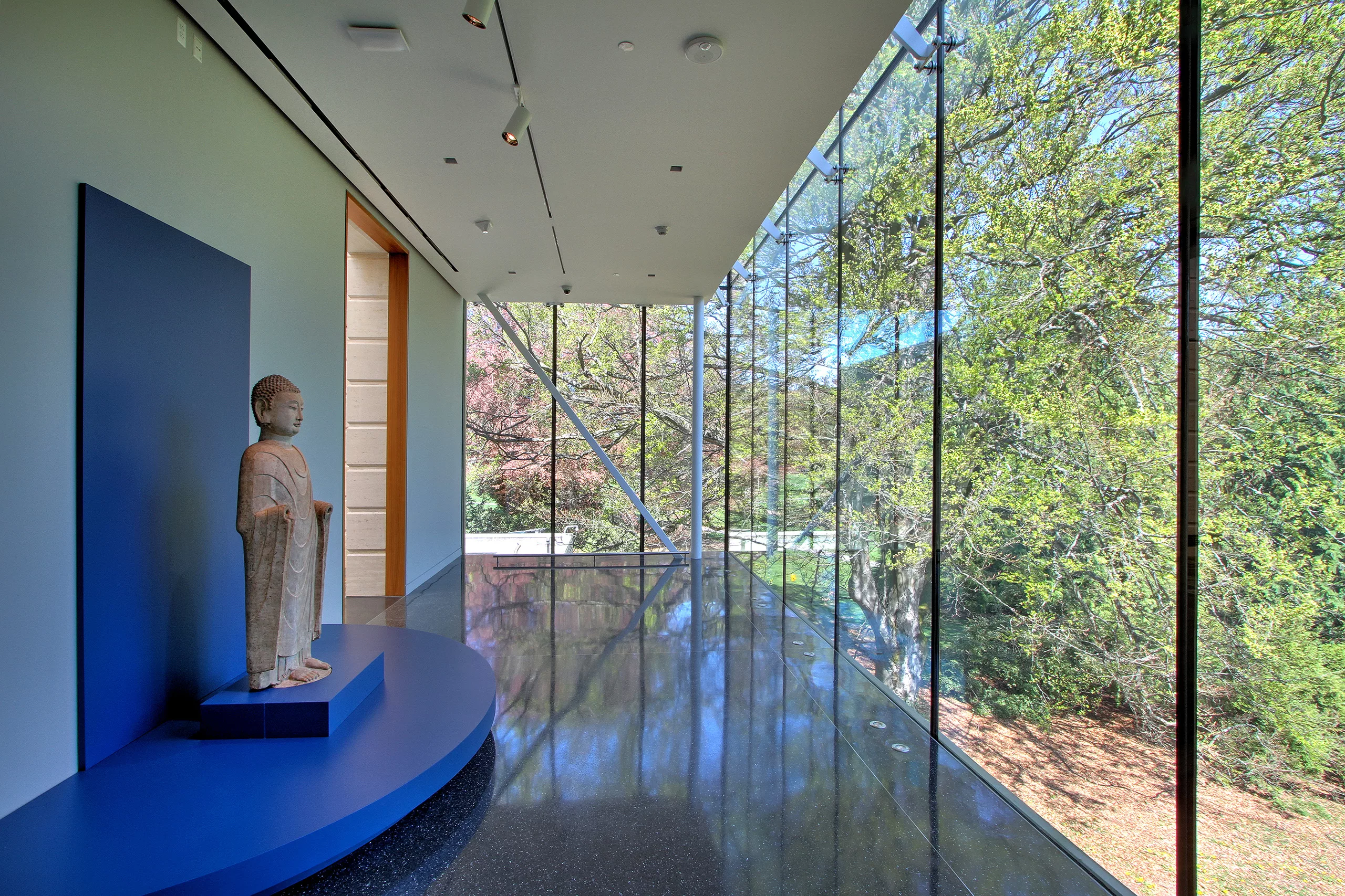 Interior of the Seattle Asian Art Museum Expansion's lobby with a marble sculpture on display and views of Volunteer Park's surrounding trees and landscape through floor-to-ceiling windows