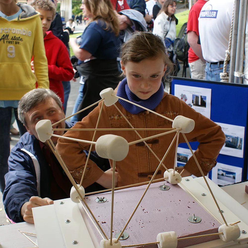 A yound girl watches her marshmallow and skewer creation on the "shake table" at a local science fair